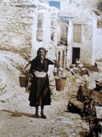09-Giovanna De Donà di ritorno dalla fontana di Gena Alta tra le case rovinate dall'incendio del '44, con il bigòl sulle spalle ed in mano il catino con i radicchi appena lavati..jpg