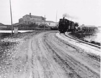 02b-Comacchio (Cappuccini), il treno proviene da Ostellato e corre sulla strada argineSpina; la chiesa dei Cappuccini è alle spalle del treno; a sx il canale provinciale.jpg